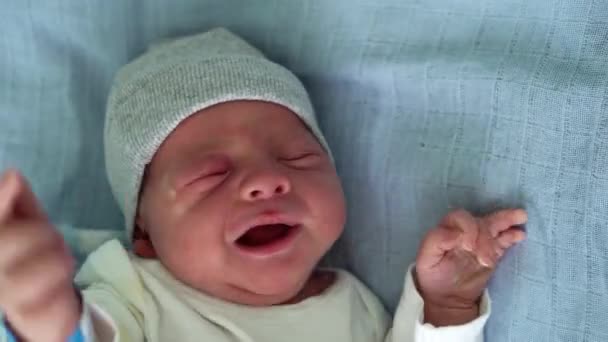 Primer plano de lindo bebé recién nacido cara roja retrato primeros días en Macro llorando sobre fondo azul. Niño al principio Minutos de la vida en sombrero. Bebés, Parto, Primeros Momentos Del Nacimiento, Principio Concepto — Vídeo de stock