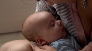 annelik, çocukluk, aile, bakım, sağlık, annelik - anne göğsü kolları üzerinde uyuyan mavi elbiseli yeni doğmuş bebekler yakın uyku. Anne öpücüklere boğuldu. Bebeği kucağına alıp evde yattı.