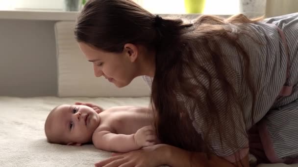 Autêntico close-up tiro jovem neo mãe mãe está brincando com nake bebê recém-nascido na cama macia branca no dia da manhã do berçário. Conceito de filhos, paternidade, infância, vida, maternidade, maternidade — Vídeo de Stock