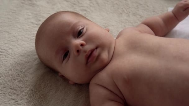 Dzieciństwo, macierzyństwo, rodzina, higiena, koncepcja niemowlęcia Close-up Happy figlarne dziecko nake 2 miesiące noworodka patrząc na aparat po kąpieli prysznic na białym miękkim łóżku. dziecko budzi się przed snem — Wideo stockowe
