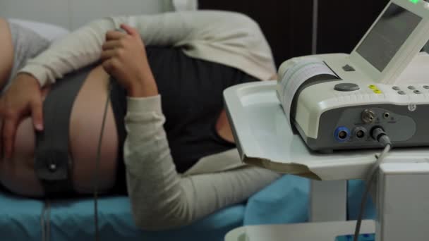 Těhotná žena bez tváře na nemocničním gauči během lékařské kontroly kardiotokografie. Navštivte gynekologa Doktor na klinice pro těhotenské poradce. Prozkoumat očekávaný břicho dítě matka zdravotní péče check up — Stock video