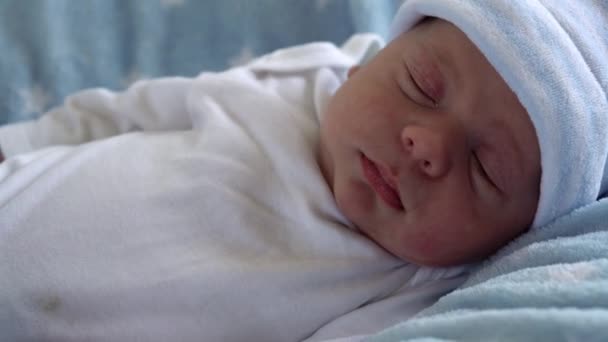 新生児の顔の肖像マクロでの初期の日目を覚ますとブルースターの背景に目を開きます.帽子の上の生活の開始時に子供。幼児、出産、誕生の最初の瞬間、概念の始まり — ストック動画