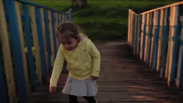 Autentyczne cute little przedszkola rodzeństwo dzieci dziewczyna i chłopiec spaceruje w parku o zachodzie słońca wiosną. Dzieciaki przeprawiają się przez stary drewniany most nad rzeką. Dzieciństwo, rodzicielstwo, rodzina, koncepcja stylu życia — Wideo stockowe