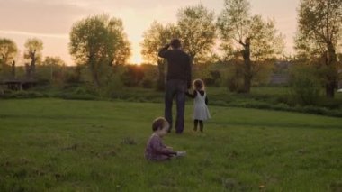 Parktaki insanlar. Gün batımında mutlu aile silueti. Baba ve bebek el ele tutuşarak zaman geçirdiler. Aileler ve eğlenceli çocuklar açık havada yürüyorlar. Babalar Günü, çocukluk, ebeveynlik kavramı.