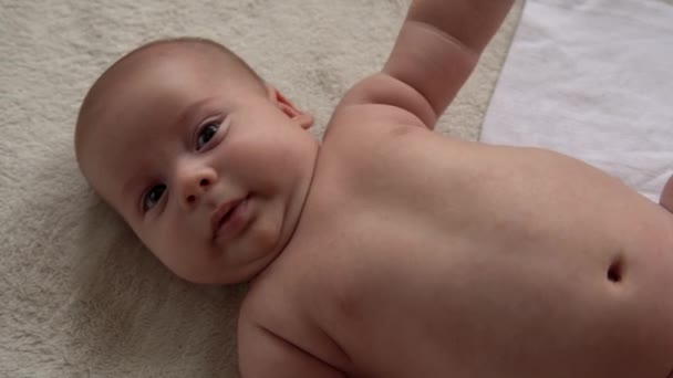 Jeugd, moederschap, familie, hygiëne, baby concept Close-up Gelukkige speelse nake kid 2 maanden pasgeboren jongen kijkend naar camera na bad douche op wit zacht bed. baby kind wakker tijd voor het slapen gaan — Stockvideo