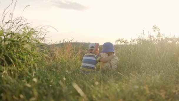 Bonito pré-escolar pequena menina e menino sentado no topo da montanha em grama alta antes do pôr do sol. Criança a caminhar no prado selvagem. Miúdo feliz nas montanhas. infância, natureza, estilo de vida, conceito de verão — Vídeo de Stock