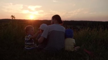 Parktaki insanlar. Mutlu aile yürüyüşleri. Babam gün batımından önce uzun otların arasında, dağın tepesinde bir sürü çocukla. Aileler ve eğlenceli çocuklar mesafeye bakarlar. Yaz, babalık, çocukluk kavramı.