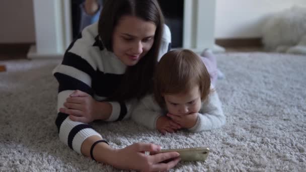 Wesoły uroczy córeczka maluch cieszyć się nauką przy użyciu smartfona z kontroli rodzicielskiej. Szczęśliwa rodzina młody rodzic matka mama pokazując śmieszne kreskówki aplikacja mobilna, oglądanie filmów relaks w domu — Wideo stockowe