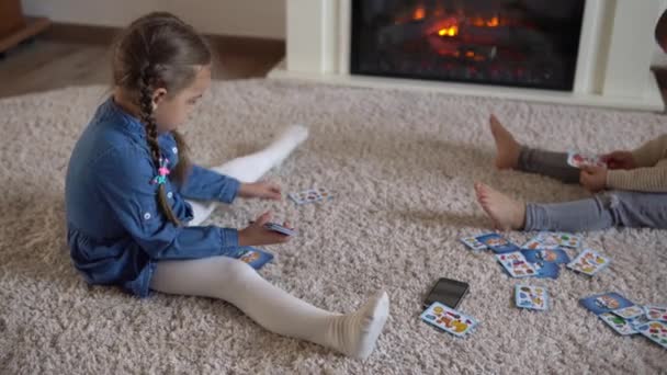 Dětství, vzdělání, hobby, rodina, přátelé, koncept přátelství. Šťastná mladá matka maminka hlídání dětí s malými předškolními dětmi tráví čas hraním karetní hry na podlaze doma u krbu — Stock video
