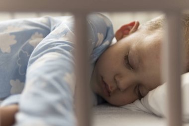 2-3 yaş arası sevimli, kreş çocuğu öğle yemeği arasında evinde yastıklı mavi pijamayla beyaz karyolada tatlı tatlı uyuyor. Çocukluk, rahatlık, rahatlık, ilaç, sağlık konsepti