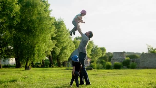 Καλοκαίρι, διακοπές, φύση, ευτυχισμένη οικογένεια, παιδική ηλικία, πατρότητα, Ημέρα του πατέρα - μπαμπάς με μικρά παιδιά προσχολικής ηλικίας τρέχει τα παιδιά παίζουν διασκεδάστε ρίξει με τα χέρια με μεγάλη φουσκωτή μπάλα στο πάρκο στο ηλιοβασίλεμα — Αρχείο Βίντεο