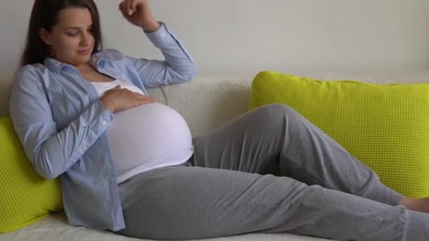 Roztomilé těhotné ženy hladí velké břicho dotýká bříško za slunečného dne. Mladý Ledy V Těhotenství Bavte se Strávit Čas Na Žluté Pohovku Doma. Mateřství, rodičovství, medicína Zdraví a péče prenatální — Stock video
