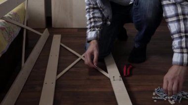 Young Black Bearded Long-haired Man Lays Out Parts Of Bookcase On Floor For Assembly Rack Furniture At Home. Collecting Wooden Boards On Living Room House. Moving At New Place. Guy Making Renovation.