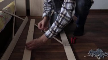Young Black Bearded Long-haired Man Lays Out Parts Of Bookcase On Floor For Assembly Rack Furniture At Home. Collecting Wooden Boards On Living Room House. Moving At New Place. Guy Making Renovation.