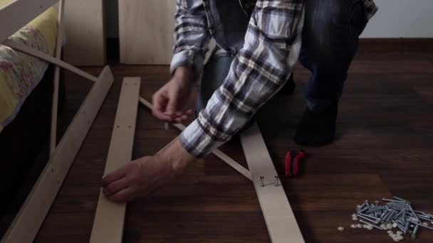 Young Black Bearded Long-haired Man Lays Out Parts Of Bookcase On Floor For Assembly Rack Furniture At Home. Collecting Wooden Boards On Living Room House. Moving At New Place. Guy Making Renovation. — Vídeo de Stock