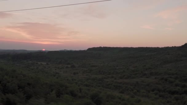 夏の背景には夕暮れ時の空の日没時に自然畑や森の風景の上の窓高速列車からの眺め。地平線に赤い夕日。交通、旅行、鉄道、通信の概念 — ストック動画