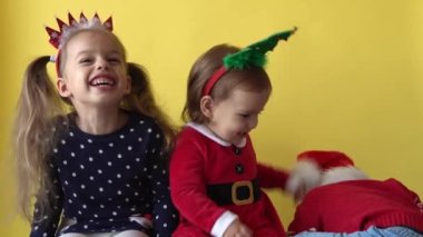 Duygusal, mutlu kardeşler, Noel Baba kıyafetiyle gezen ve sarı arka plandaki kameraya bakan bebek çocuk. Doğum gününü kutlayan çocuk Noel Sahnesi oynuyor. Çocuk Yılbaşını Eğlenerek Geçiriyor