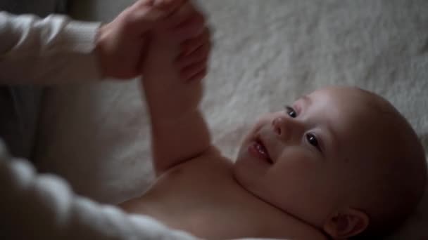 Bebé recién nacido y mamá joven yacen en la cama. Lindo retrato de cara de niño sin dientes sonriente. Mujer hace masaje desnudo niño. Mamá cuida de Babe. Bebés, Día de la Madre, Parto, Principio, Concepto de Relación — Vídeo de stock