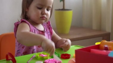 Çocuklar için heykel ve kil modelleme. 2-5 yaşlarındaki kız pembe oyun hamurunu parmaklarıyla ve plastik maket bıçağıyla şekillendiriyor. Oyun kilini kullanarak iyi motor becerileri ve çocuk yaratıcılığını geliştirmek.