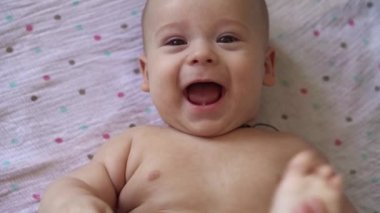 Küçük çıplak bebek bezi komik gülümsüyor, sırtüstü yatıyor. Ayak parmaklarını ısıran neşeli, enerjik çocuk portresi. Ayak masajı yapan çocuk doktorları. Basit egzersiz kemikleri, güçlü kaslar.