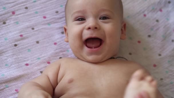 Kleine Naakte luier pasgeboren baby is grappig lachend, liggend achterin. Portret van vrolijk speels energiek kind bijtende tenen voeten massage geneeskunde pediatrie doen eenvoudige oefening botten spieren sterker — Stockvideo