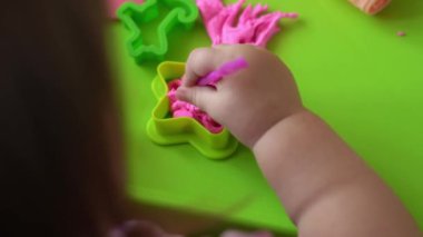 Çocuklar için heykel ve kil modelleme. 2-5 yaşlarındaki kız pembe oyun hamurunu parmaklarıyla ve plastik maket bıçağıyla şekillendiriyor. Oyun kilini kullanarak iyi motor becerileri ve çocuk yaratıcılığını geliştirmek.