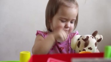 Küçük kız evde oyuncak ayıyla oynarken komik ifadesiz suratını ekşitiyor. Çocukluk duyguları, üzüntü, mutluluk. yaramaz kaprisli çocuk. Çocuk pencereden dışarı bakıyor.
