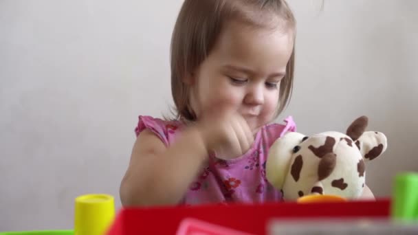Liten Toddler flicka gör roliga uttrycksfulla grimace ansikte leka med mjuk leksaksbjörn hemma. Barndomskänslor sorg lycka. Styggt nyckfullt barn. Närbild unge tittar ut punkt till fönster — Stockvideo