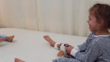 İki gülümseyen anaokulu çocuğu pijamalarıyla yatakta oyuncak ayıyla oynuyorlar. Kardeşler Küçük İkiz Oğlan ve Kız Eğleniyor. Evde karantinada mutlu çocuklar. Arkadaşlık, Aile, Eğitim Konsepti