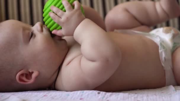 Οικογένεια, παιδιά. Κοντινό πλάνο Happy baby baby with Teething Toy. Γυμνό μικρό παιδί σε πάνα παίζει με πράσινη λαστιχένια μπάλα πίσω στο σπίτι. Παιδιατρική Φροντίδα Νεογνών — Αρχείο Βίντεο