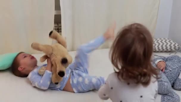 Two Smiling Preschool Toddler Children In Pajamas Playing With Teddy Bear on Bed. Siblings Little Twins Boy and Girl Have Fun. Happy Kids On Quarantine At Home. Friendship, Family, Education Concept — Stock Video