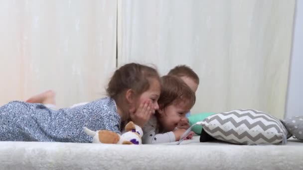 Niños de preescolar sonrientes en pijama viendo dibujos animados en el teléfono inteligente en la cama. Los hermanos Little Twins Boy y Girl se divierten. Niños felices en cuarentena en casa. Amistad, Familia, Educación — Vídeos de Stock