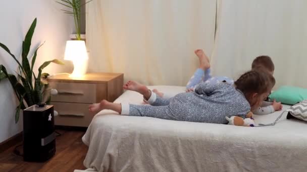 Niños de preescolar sonrientes en pijama viendo dibujos animados en el teléfono inteligente en la cama. Los hermanos Little Twins Boy y Girl se divierten. Niños felices en cuarentena en casa. Amistad, Familia, Educación — Vídeo de stock