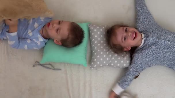 Dos niños de preescolar sonrientes en pijama jugando con el oso de peluche en la cama. Los hermanos Little Twins Boy y Girl se divierten. Niños felices en cuarentena en casa. Amistad, Familia, Concepto de Educación — Vídeos de Stock