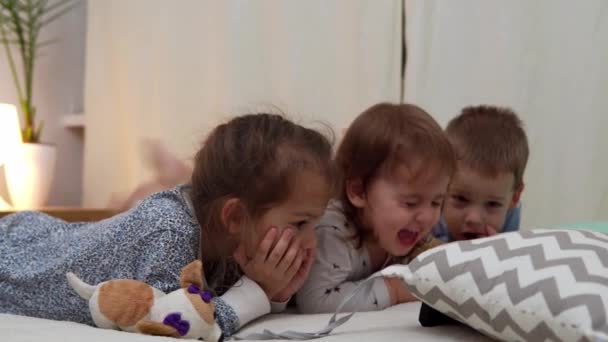 Crianças pré-escolares sorridentes em pijamas assistindo desenhos animados no smartphone na cama. Irmãozinhos gêmeos menino e menina divirtam-se. Crianças felizes em quarentena em casa. Amizade, Família, Educação — Vídeo de Stock