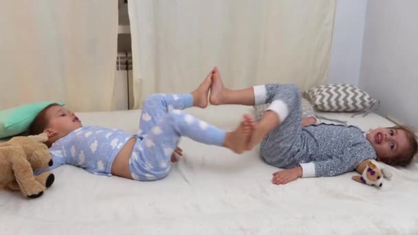 Dwoje uśmiechniętych dzieci w piżamie bawiących się z misiaczkiem w łóżku. Rodzeństwo Little Twins Boy and Girl Have Fun. Szczęśliwe dzieci na kwarantannie w domu. Przyjaźń, Rodzina, Pojęcie edukacji — Wideo stockowe
