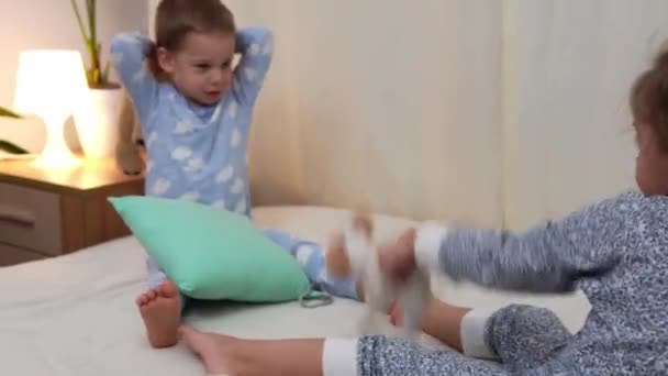 Duas crianças pré-escolares sorridentes em pijamas brincando com ursinho de pelúcia na cama. Irmãozinhos gêmeos menino e menina divirtam-se. Crianças felizes em quarentena em casa. Amizade, Família, Conceito de Educação — Vídeo de Stock