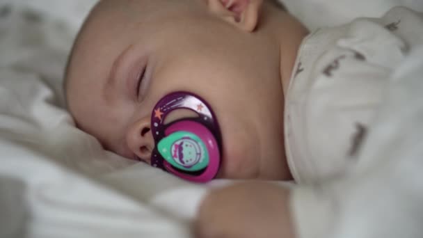 Kindertijd, kindertijd, ontwikkeling, geneeskunde en gezondheid concept - close-up gezicht van pasgeboren mollig slapende baby 6 maanden met fopspeen liggend op de maag bedekt met deken op bed op witte achtergrond. — Stockvideo