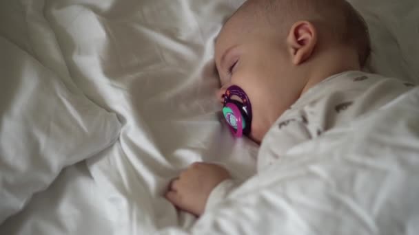 Kojenectví, dětství, vývoj, medicína a zdravotní koncepce - detailní tvář novorozence baculaté spící miminko 6 měsíců s dudlíkem ležícím na břiše přikryté přikrývkou na lůžku na bílém pozadí. — Stock video
