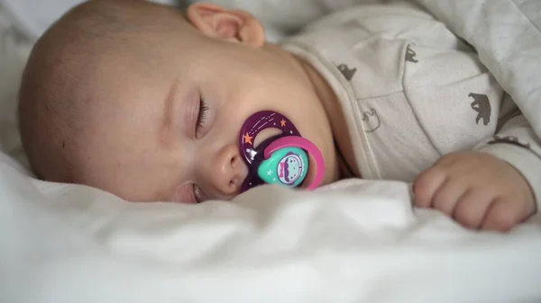 Βρεφική ηλικία, παιδική ηλικία, ανάπτυξη, ιατρική και υγεία έννοια - close-up πρόσωπο του νεογέννητου παχουλό μωρό ύπνου 6 μήνες με πιπίλα που βρίσκεται στο στομάχι καλύπτονται με κουβέρτα στο κρεβάτι σε λευκό φόντο. — Φωτογραφία Αρχείου