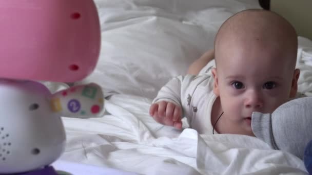 Primer plano Feliz niño juguetón de 6 meses de edad. Niño recién nacido mirando a la cámara después de la ducha de baño en la cama blanda blanca. bebé niño despertando antes de acostarse con Toy. Infancia, maternidad, familia, concepto infantil — Vídeos de Stock