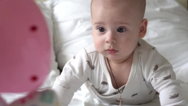 Κοντινό πλάνο Ευτυχισμένο παιχνιδιάρικο παιδί 6 μηνών. Νεογνό αγόρι κοιτάζει κάμερα μετά το μπάνιο ντους σε λευκό μαλακό κρεβάτι. το μωρό ξυπνάει πριν κοιμηθεί με τον Τόι. Παιδική ηλικία, μητρότητα, οικογένεια, νήπιο — Αρχείο Βίντεο