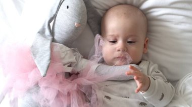 Yakın plan Mutlu neşeli çocuk 6 aylık. Yeni doğan çocuk, beyaz yumuşak yatakta banyo sonrası kameraya bakıyor. Bebek oyuncakla yatmadan önce uyandı. Çocukluk, annelik, aile, bebek konsepti