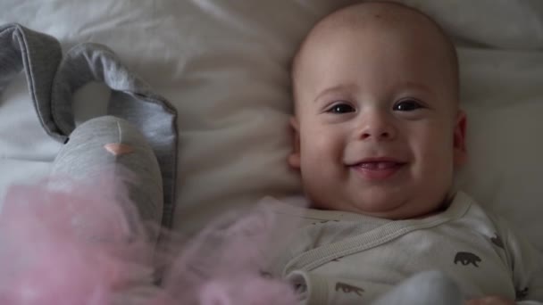 Close-up Vrolijk speels kind van 6 maanden oud. Pasgeboren jongen kijkt naar camera na bad douche op wit zacht bed. baby kind wakker tijd voor het slapen gaan met Toy. Jeugd, moederschap, familie, kinderconcept — Stockvideo