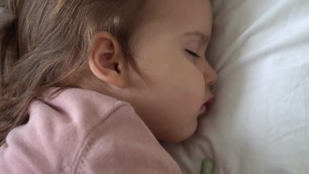Автентична мила дівчинка спить солодко в зручному білому та сірому ліжку крупним планом. Красива втомлена дитина відпочиває дбайливо заспокоює. Малюк у ліжечку. Догляд, дитинство, батьківство, концепція життя — стокове відео