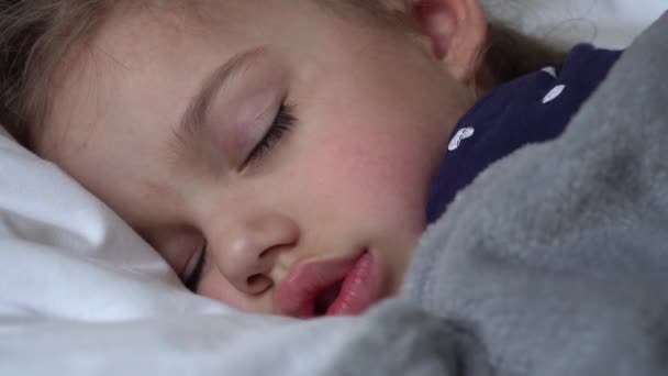 Автентична мила дівчинка спить солодко в зручному білому та сірому ліжку крупним планом. Красива втомлена дитина відпочиває дбайливо заспокоює. Малюк у ліжечку. Догляд, дитинство, батьківство, концепція життя — стокове відео