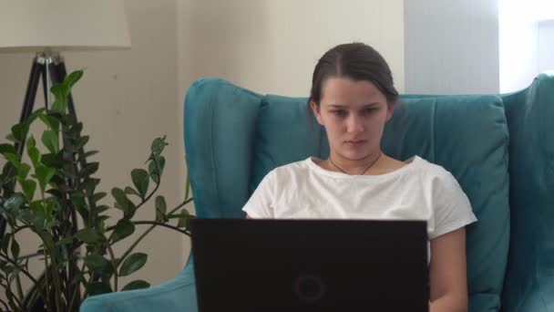 リビングルームのラップトップで本物の若い女性のチャット.ITを使って検索を書く。快適な簡単な椅子でインターネットを閲覧するコンピュータ上で働く幸せな女性。ビジネス、教育、テクノロジーの概念 — ストック動画