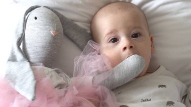 Yakın plan Mutlu neşeli çocuk 6 aylık. Yeni doğan çocuk, beyaz yumuşak yatakta banyo sonrası kameraya bakıyor. Bebek oyuncakla yatmadan önce uyandı. Çocukluk, annelik, aile, bebek konsepti