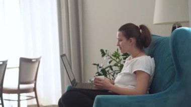 Oturma odasında dizüstü bilgisayarla konuşan otantik bir genç kadın. Kullanarak Yazma Araması. Bilgisayarda çalışan mutlu bayan rahat rahat koltukta interneti tarıyor. Buisenes, Eğitim, Teknoloji Konsepti