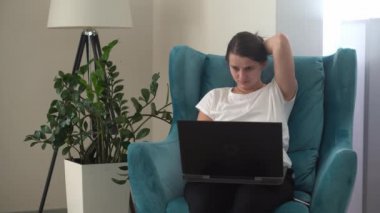 Oturma odasında dizüstü bilgisayarla konuşan otantik bir genç kadın. Kullanarak Yazma Araması. Bilgisayarda çalışan mutlu bayan rahat rahat koltukta interneti tarıyor. Buisenes, Eğitim, Teknoloji Konsepti
